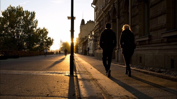Persona adulta caminando por una calle amplia con edificios y luz suave